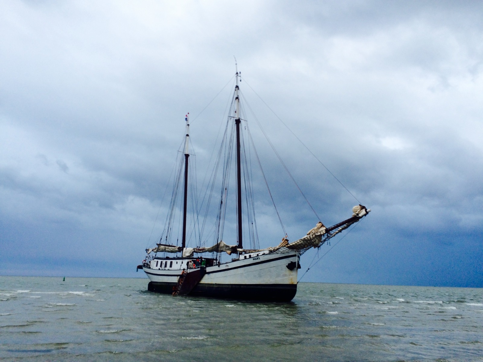Three-masted traditional sailing ship under dramatic storm clouds