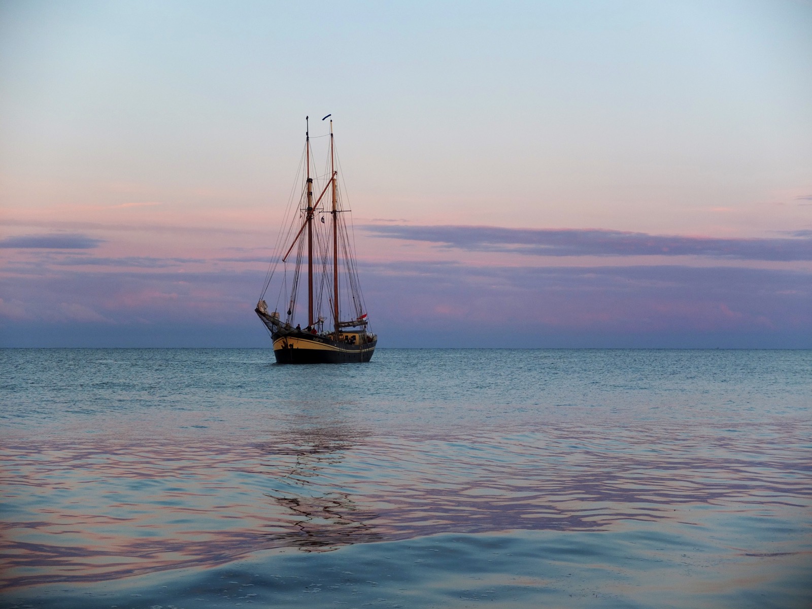 Traditional two-masted sailing ship anchored on calm sea at sunset