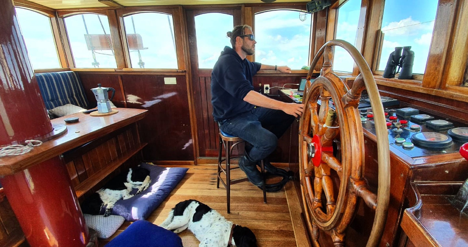 Fabio Andreatta in the wooden wheelhouse of a traditional ship with dogs resting nearby